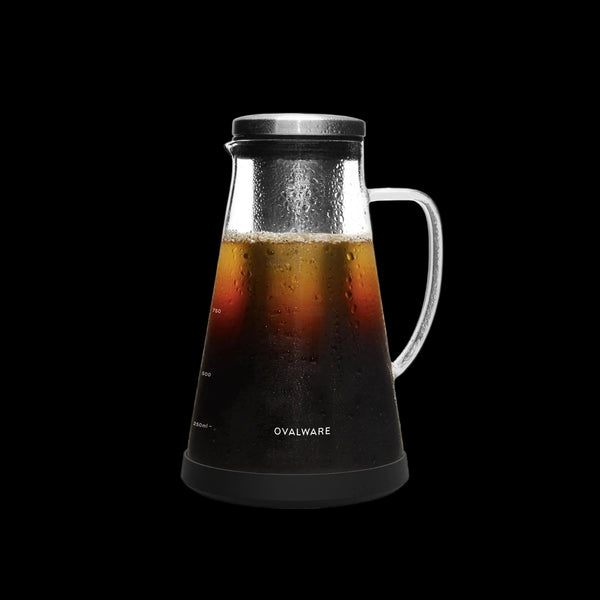 Glass carafe with black base and lid filled with iced coffee, brand 'Ovalware' visible.